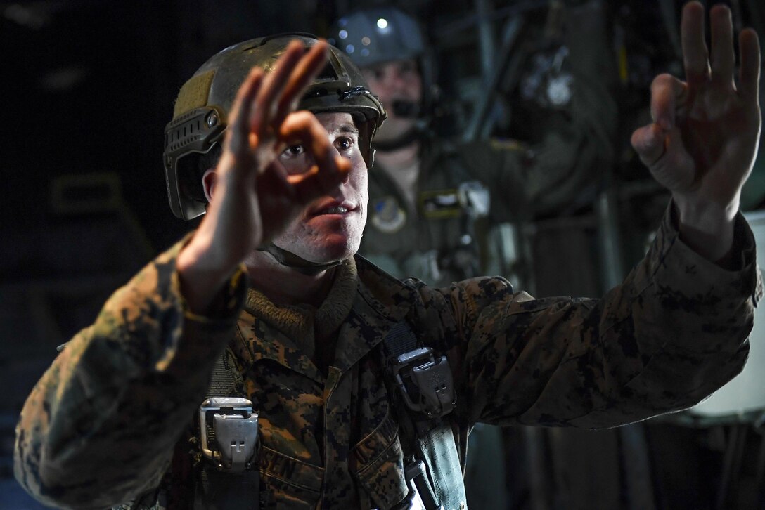 A Marine uses hand signals to instruct fellow Marines while flying in a C-130 Hercules before participating in a static line parachute jump over Yokota Air Base, Japan, Jan. 11, 2017. The Marine is a jump master assigned to the 3rd Marine Division's 3rd Reconnaissance Battalion, 3rd Marine Expeditionary Force. Air Force photo by Airman 1st Class Donald Hudson 