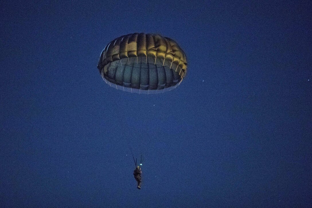 A Marine descends to the drop zone after exiting from an Air Force C-130 Hercules participating in a night static line parachute jump over Yokota Air Base, Japan, Jan. 11, 2017. Air Force photo by Yasuo Osakabe