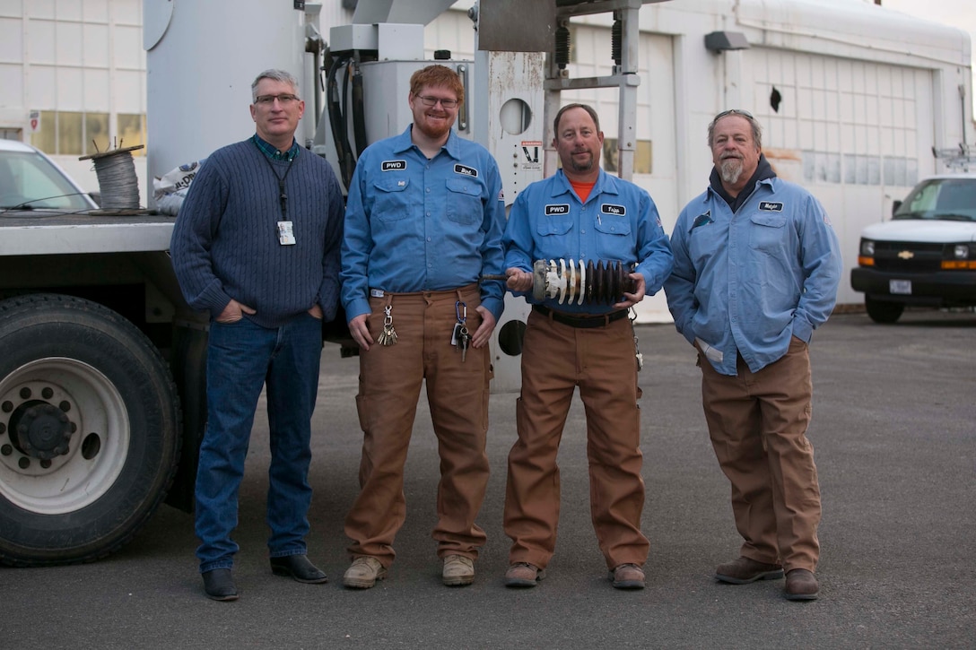 Garry Morrissett, utilities and energy management supervisor, Richard Birt, Kelly Trippa and Bill Motzko, mechanics, Public Works Division, hold the broken transformer that caused a power outage aboard Marine Corps Air Ground Combat Center, Twentynine Palms, Calif., Jan. 12, 2016. Morrissett, Birt, Trippa and Motzko were among the five men who worked to repair the power outage on New Years’ Day. (Official Marine Corps photo by Cpl. Thomas Mudd/Released)