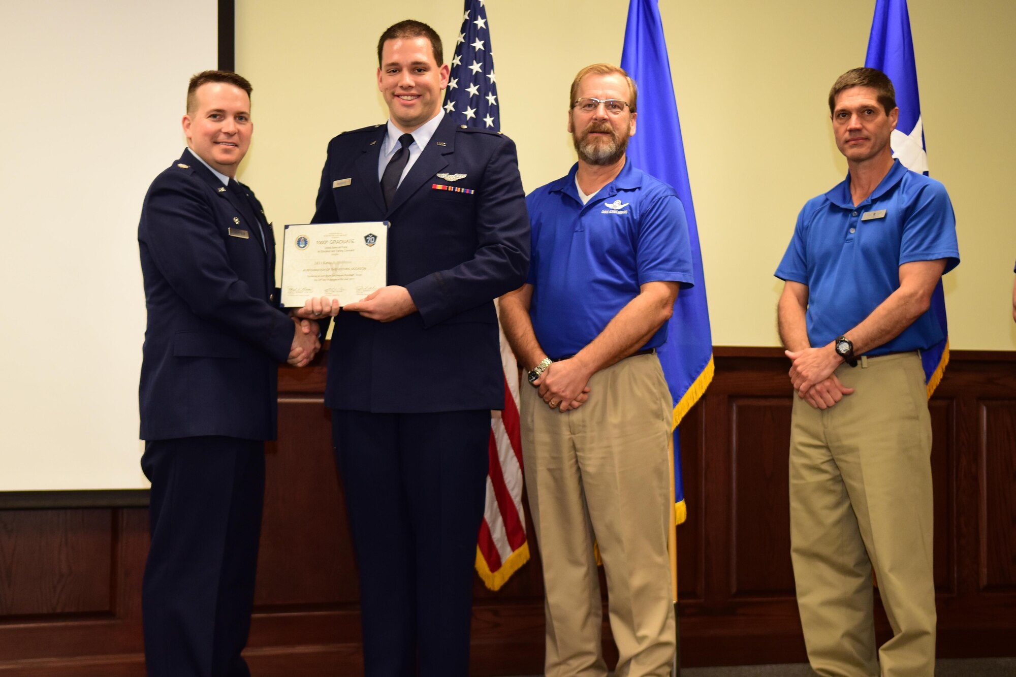 Lt. Col. Jason Thompson, 558th Flying Training Squadron Commander, presents a certificate to the thousandth Undergraduate Remotely Piloted Aircraft Training graduate, 2nd Lt. Kevin, during a graduation ceremony Jan 20th at Joint Base San Antonio-Randolph, Texas. Chris Schweinberg and James Taylor, were both cadre members when the URT program grew to become a squadron in 2010. (U.S. Air Force photo illustration by Randy Martin) 