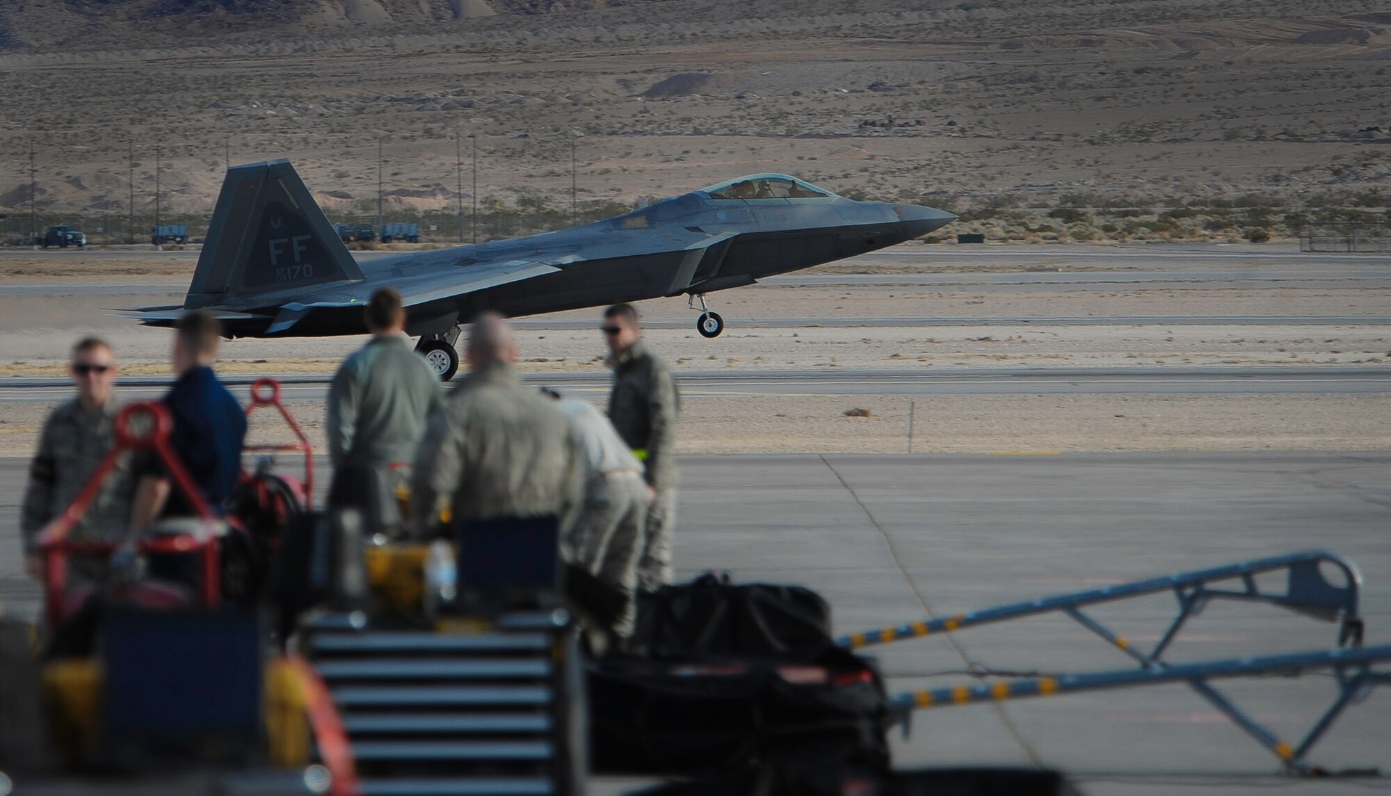 An F-22 Raptor assigned to the 1st Fighter Wing, Joint Base Langley-Eustis, Va., lands as maintainers wait for the fighter to taxi before Red Flag 17-1 on Nellis Air Force Base, Nev., Jan. 18, 2017. All four branches of the U.S. Military and air forces from allied nations participate in Red Flag. (U.S. Air Force photo by Airman 1st Class Kevin Tanenbaum/Released)