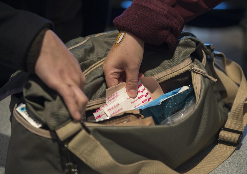 Participants of a Noncombatant Evacuation Operation Townhall meeting inspect the contents of a NEO kit, a bag used to carry documentation, rations, medication and other essentials in case of an immediate disaster or evacuation, Jan. 23, 2017, at Yokota Air Base, Japan. NEO is a mandatory or voluntary departure of civilian noncombatants and nonessential military personnel from danger in an overseas country. (U.S. Air Force Photo by Airman 1st Class Juan Torres)