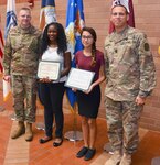 Brig. Gen. Jeffrey Johnson (left), Brooke Army Medical Center commanding general, and BAMC Command Sgt. Maj. Albert Crews (right) present certificates of appreciation to students Avea Walters (second from left) and Seleste Cavazos (second from right) for reading their essays about Martin Luther King Jr. Jan. 18 during the Martin Luther King Jr. observance in the Medical Mall.