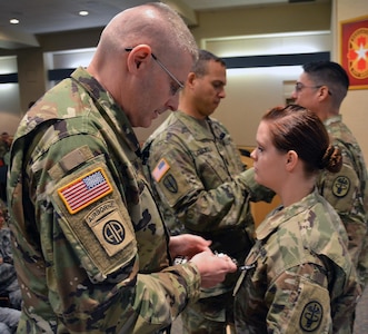 Brig. Gen. Jeffrey Johnson (left), Brooke Army Medical Center commanding general, presents Spc. Brittany Lopez (second from right), Army healthcare specialist, with a black badge as BAMC Command Sgt. Maj. Albert Crews (second from left) presents Staff Sgt. Alfredo Herrera Jr. (right), noncommissioned officer in charge of 2 East, his black badge during the 68W Utilization Program kick-off ceremony Jan. 17 in the fourth-floor auditorium. The black badge signifies the wearer possesses the basic skills of a 68W. 