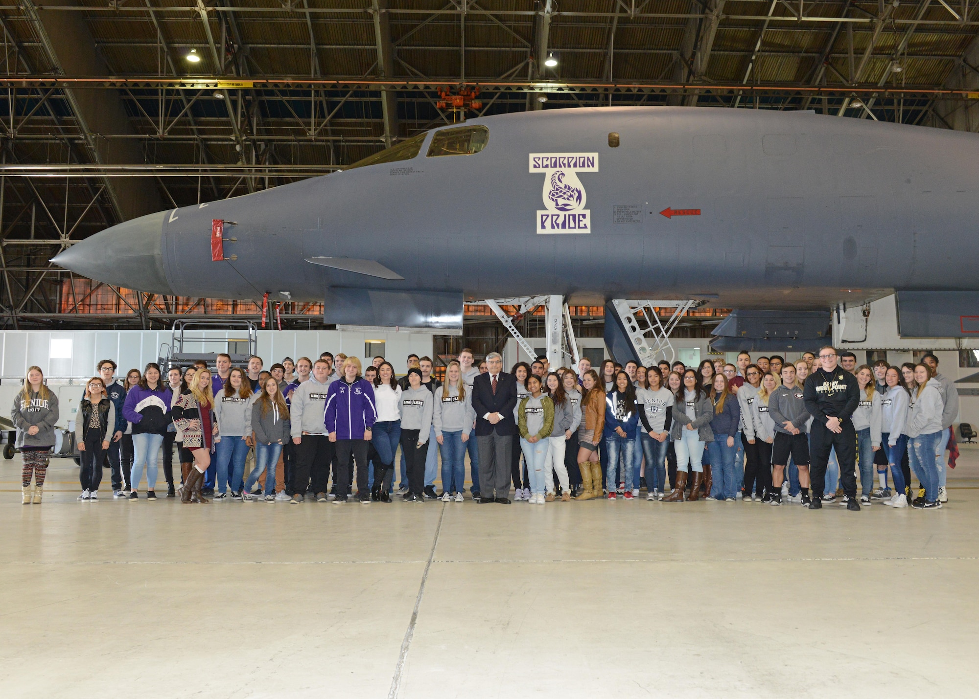 Mike Machat (center), aviation artist, poses for a photo with Desert Junior-Senior High School seniors Jan. 13 in Hangar 1210. The school’s Class of 2017 was invited out to see the nose art painted on a B-1 Lancer in honor of the base high school. Students took class and yearbook photos in front of the bomber. (U.S. Air Force photo by Kenji Thuloweit)