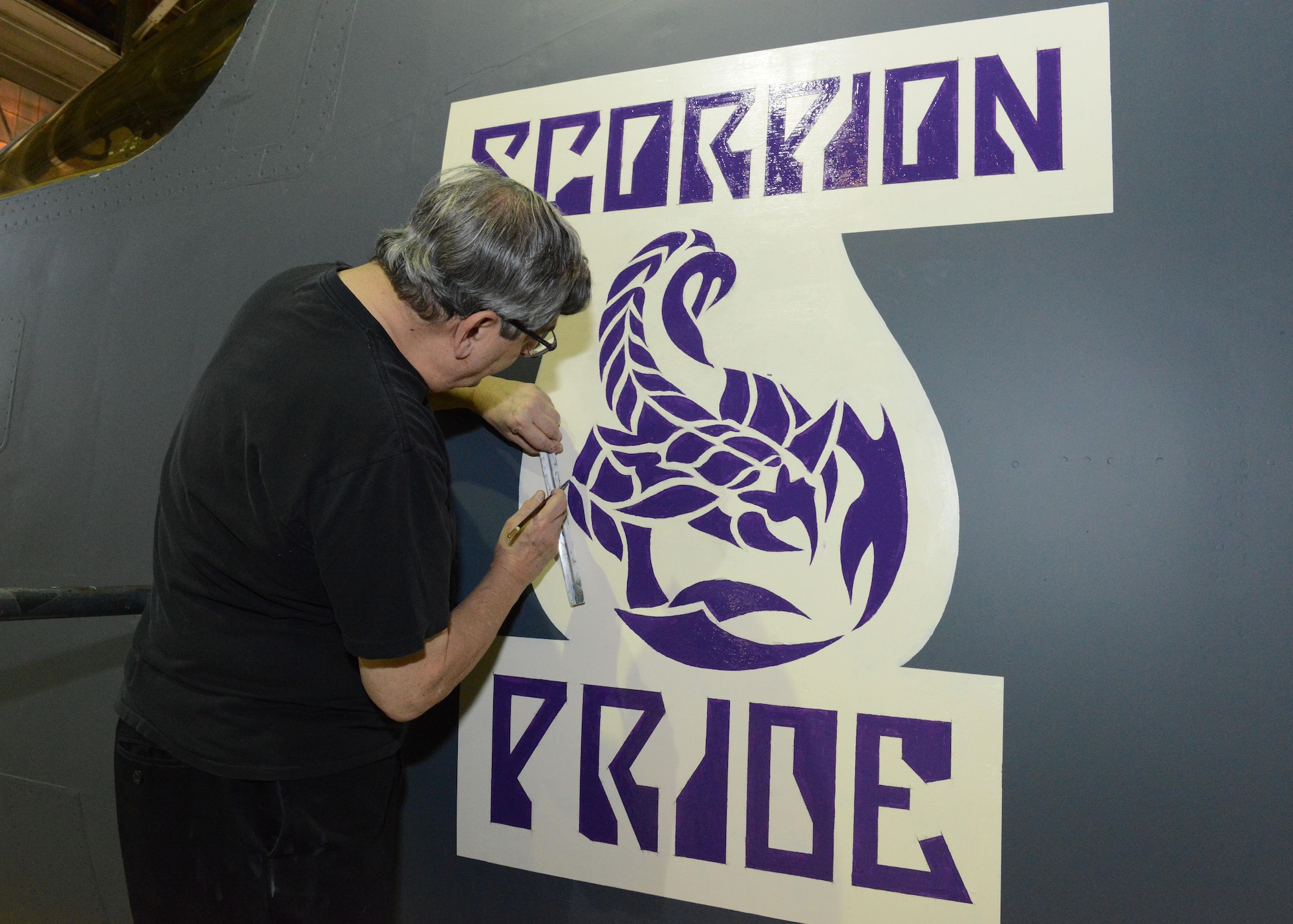 Mike Machat, aviation artist, puts the finishing touches on a Desert Junior-Senior High School logo on a 419th Flight Test Squadron B-1 Lancer Dec. 13, 2016. Seniors of DHS Class of 2017 were invited to Hangar 1210 Jan. 19 to tour the plane and take class photos with it. (U.S. Air Force photos by Kenji Thuloweit)