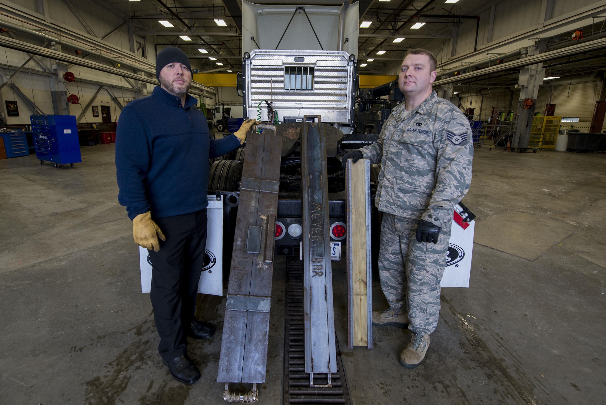 Staff Sgt. Joshua Meyer, 375th Logistics Readiness Squadron vehicle operations control center NCOIC, and Teddy Manning, 375th LRS chief of personal property, show the different iterations of the Meyer’s Bar as it has been continuously being tweaked Jan. 19 at Scott Air Force Base, Ill. The “Meyers Bar 2.0” is a 5-foot reinforced steel bar that has been constructed to support a lowboy trailer’s hydraulic gooseneck hitch to prevent it from bending. (U.S. Air Force photo/Senior Airman Joshua Eikren)