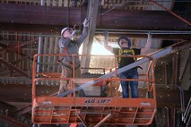 Loyd Redus, (left) Faith Technologies foreman and Kaleb Humphery, Faith Technologies apprentice, install conduits for the fans on the ceiling of Hangar 285 Jan. 24, 2017, at Altus Air Force Base Oklahoma. The new fans improve air circulation in hangars and aim to keep the maintenance working conditions safe, controlling health and temperature concerns and enabling the maintainers to work on aircraft year-round. (U.S. Air Force photo by Airman 1st Class Cody Dowell/released)