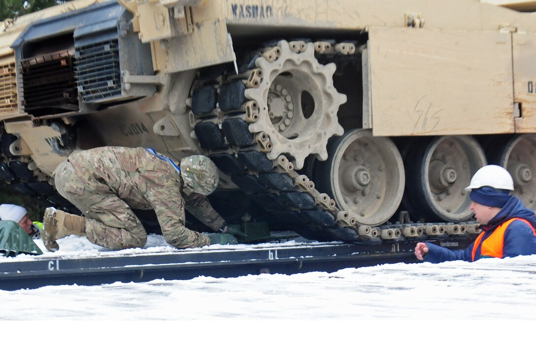 A soldier places a block under the tread of an M1A2 Abrams tank in Zagan, Poland, Jan. 25, 2017, to secure the tank for transport via rail to Grafenwoehr, Germany. Army photo by Staff Sgt. Corinna Baltos