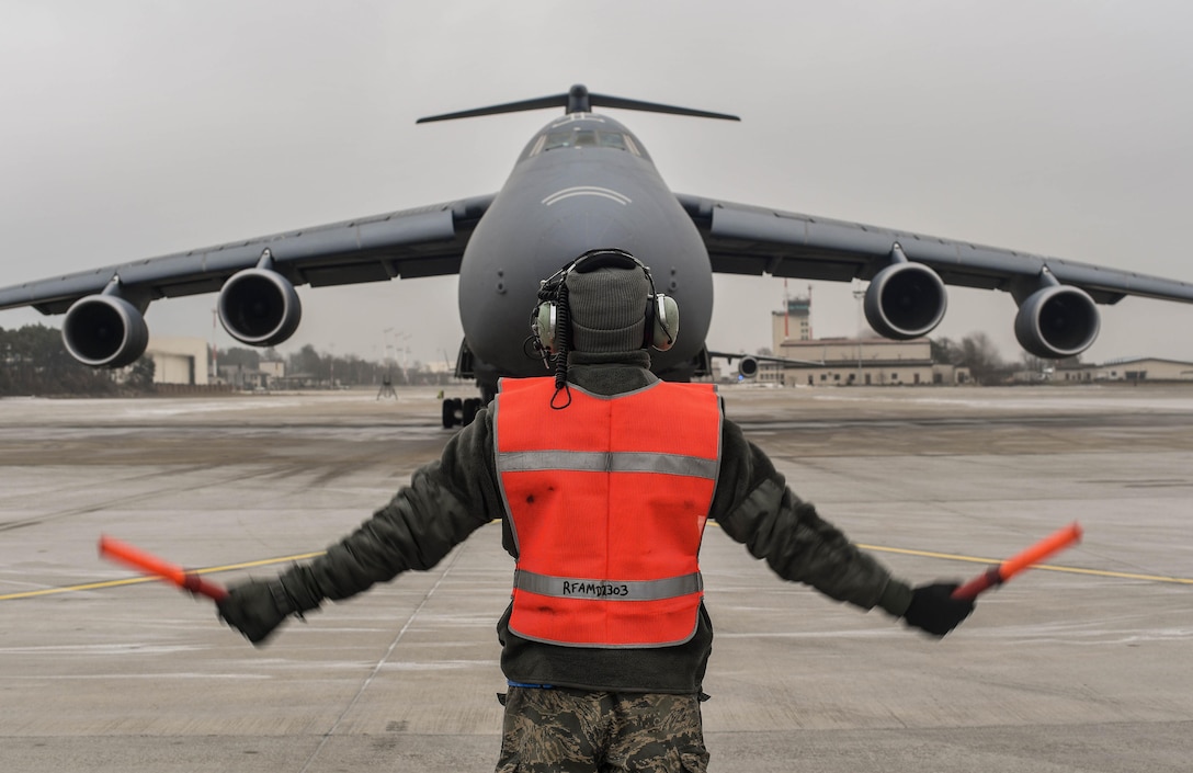 Senior Airman Earl Shelton, 721st Aircraft Maintenance Squadron aerospace maintenance technician, marshals a C-5M Super Galaxy into place at Ramstein Air Base, Germany, Jan. 24, 2017. After it was in place, 721st AMXS Airmen chocked the wheels, plugged it into a generator, checked tire pressure, refilled oil, and refueled the aircraft. On average, the 721st AMXS inspects, services, and repairs 30 aircraft in a single day, as part of the 521st Air Mobility Operations Wing at Ramstein.  (U.S. Air Force photo by Senior Airman Tryphena Mayhugh)