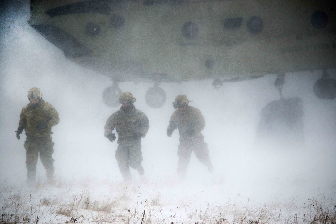 Soldiers rush away from a CH-47 Chinook helicopter after attaching a large bundle underneath during slingload training at the Baumholder Military Training Area in Baumholder, Germany, Jan. 26, 2017. Army photo by Erich Backes