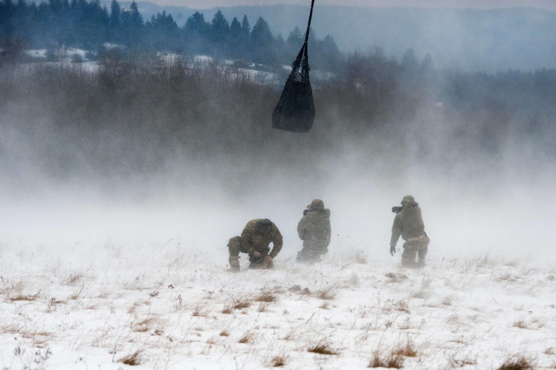 Soldiers take cover as a CH-47 Chinook helicopter lifts off with a large bundle underneath during slingload training at the Baumholder Military Training Area in Baumholder, Germany, Jan. 26, 2017. Army photo by Erich Backes