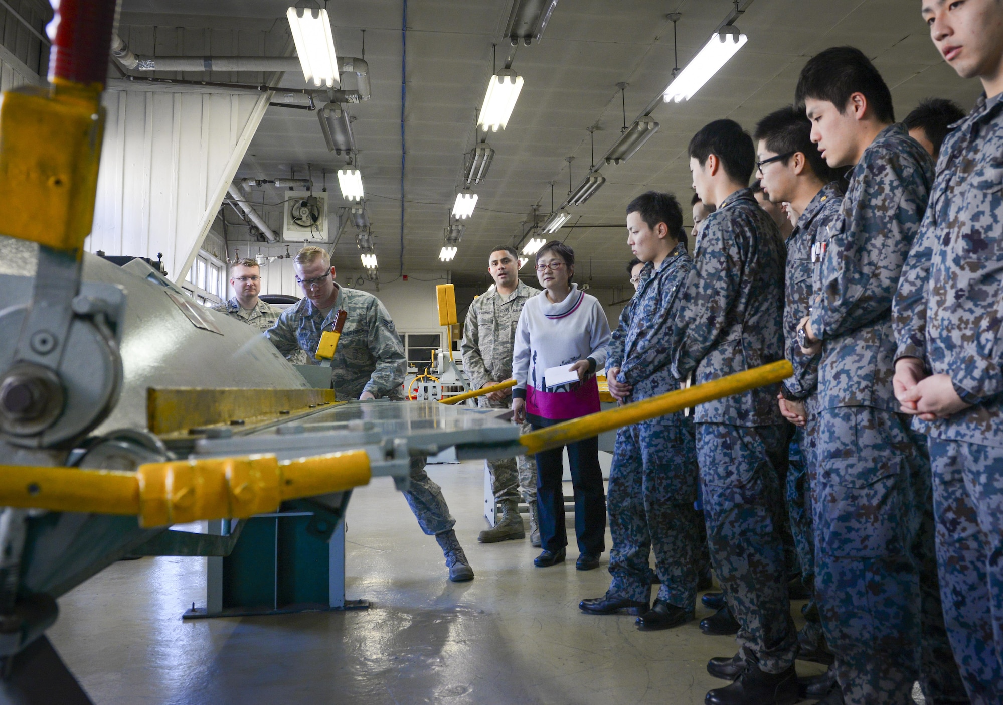 Senior Airman Douglas Smith, 374th Maintenance Squadron fabrication flight aircraft structural journeyman, demonstrates a machine for cutting sheet metal to Japan Air Self Defense Force maintenance officers-in-training at Yokota Air Base, Japan, Jan. 25, 2017.  The officers-in-training interacted with Yokota Airmen, asked questions and witnessed firsthand how maintenance operates at Yokota. Interactive bilateral visits are designed to strengthen Japan-U.S. relations and improve how they operate together. (U.S. Air Force photo by Senior Airman Elizabeth Baker)