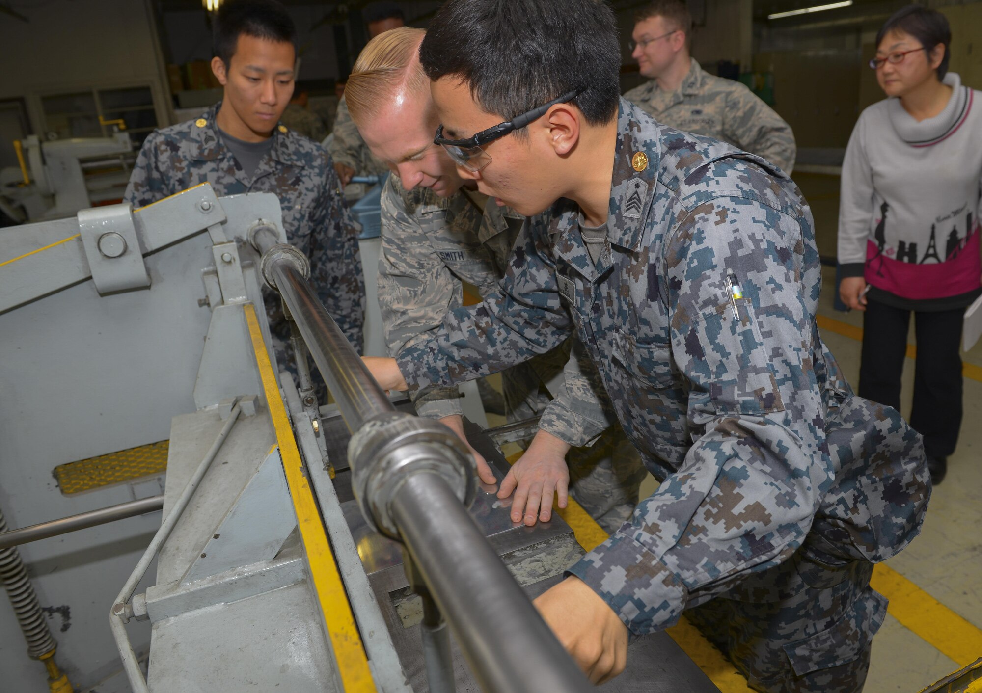 A Japan Air Self Defense Force maintenance officer-in-training operates a sheet metal cutting machine with help from Senior Airman Douglas Smith, 374th Maintenance Squadron fabrication flight aircraft structural journeyman, at Yokota Air Base, Japan, Jan. 25, 2017. Interactive bilateral visits are designed to strengthen Japan-U.S. relations and improve how they operate together. (U.S. Air Force photo by Senior Airman Elizabeth Baker)