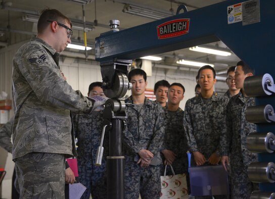 Senior Airman Nicholas Barnes, 374th Maintenance Squadron fabrication flight aircraft structural journeyman, demonstrates a sheet metal crimping machine at Japan Air Self Defense Force maintenance officers-in-training at Yokota Air Base, Japan, Jan. 25, 2017. The JASDF officers visited Yokota maintenance shops and discovered how Yokota MXG operates in order to understand and learn from their differences. Interactive bilateral visits are designed to strengthen Japan-U.S. relations and improve how they operate together. (U.S. Air Force photo by Senior Airman Elizabeth Baker)