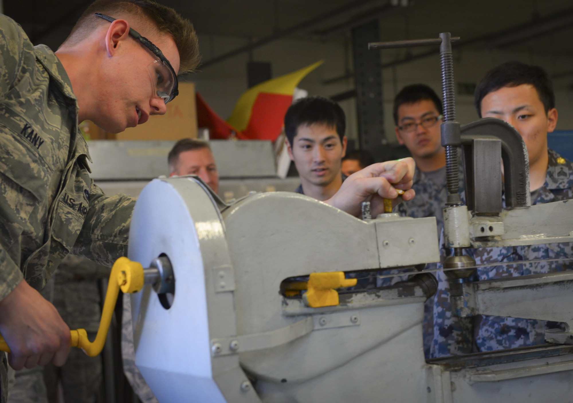 Airman 1st Class Frank Kany, 374th Maintenance Squadron fabrication flight aircraft structural journeyman, demonstrates a machine for cutting holes in sheet metal at Japan Air Self Defense Force maintenance officers-in-training at Yokota Air Base, Japan, Jan. 25, 2017. The officers-in-training interacted with Yokota Airmen, asked questions and witnessed firsthand how maintenance operates at Yokota. Interactive bilateral visits are designed to strengthen Japan-U.S. relations and improve how they operate together. (U.S. Air Force photo by Senior Airman Elizabeth Baker)
