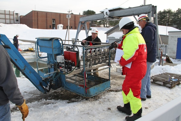 Researchers prepare a boom with a hopper attachment that conveys/drops herder/igniter tubes into a basin at the Engineer Research and Development Center’s Cold Regions Research and Engineering Laboratory, recently.