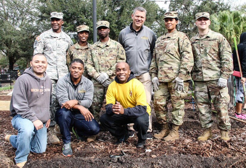 Soldiers from the 143d Sustainment Command (Expeditionary) pose for a group photo with National Football League legends Mark Brunell (top row, third from right) and Warrick Dunn (bottom row, second from left) Jan. 27, 2017, at the Colonialtown North Community Garden in Orlando, Fla. The Army Reserve and the NFL joined forces to lighten the environmental impact produced the first ever Pro Bowl to take place in Orlando by bringing one of the city’s oldest community gardens back to its former, greener glory. The players and Soldiers worked side-by-side with scores of other volunteers from Central Florida to pour mulch, plant trees, repair fences and build garden beds. 