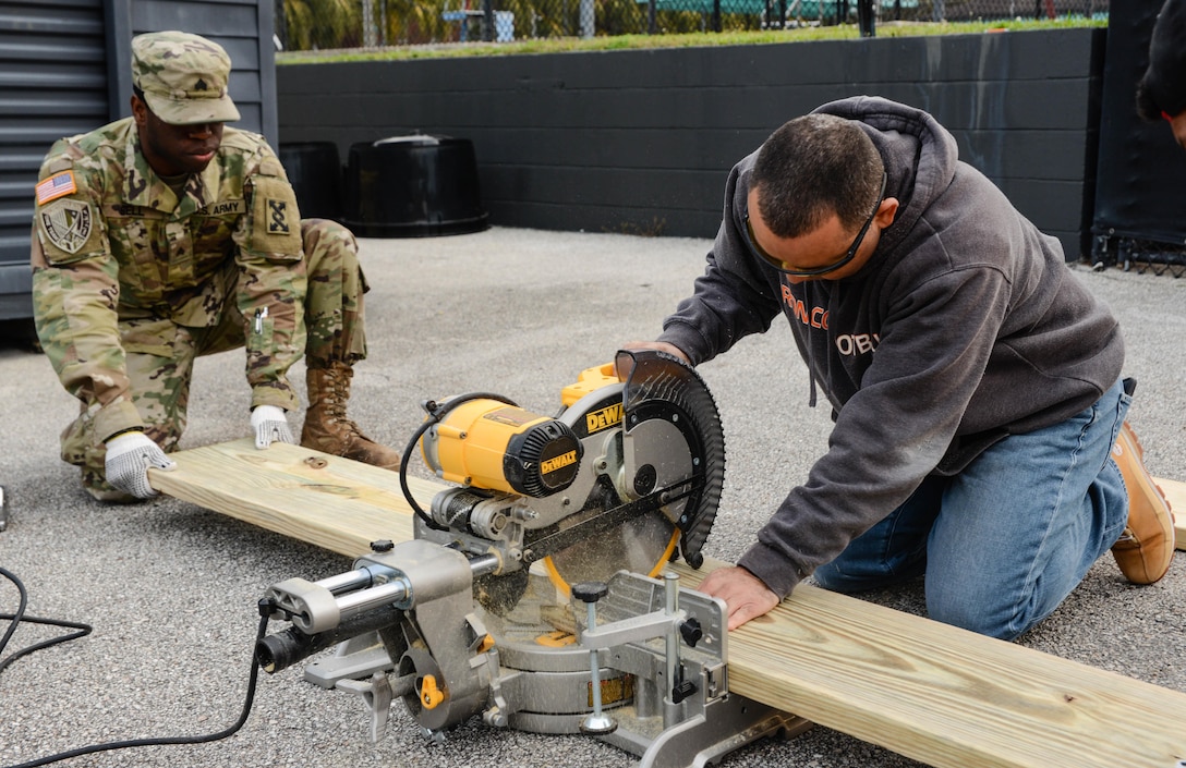 Army Warrant Officer Candidate Brian M. Torres (right), a Vineland, N.J., native who recently entered the warrant officer candidate program while serving in the 143d Sustainment Command (Expeditionary)’s G6 (Communications) section, operates a chop saw while Army Sgt. Jonathan Bell (left), an Orlando, Fla., native serving as a human resources noncomissioned officer, Headquarters & Headquarters Company, 143d ESC, holds the wooden board in place during a an environmental sustainability community project Jan. 27, 2017, in Orlando, Fla. Bell, Torres and five other Army Reserve Soldiers constructed several wooden garden beds to help revive  Orlando’s Colonialtown North Community Garden to its former, greener glory. Directed by Green Works Orlando in conjunction with the NFL’s Environmental Program, the garden’s revival was one of the many community projects both organizations managed to lighten the environmental footprint produced by the tens of thousands of football fans who have flocked to The City Beautiful to watch the NFL’s first Pro Bowl game to take place in the Continental U.S. since 1979. 