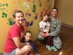 The Daniels family pose in front of the radiation treatment room’s victory wall, with the hand prints of everyone who has gone through treatment in that room. The Daniels family’s hand prints are between them.