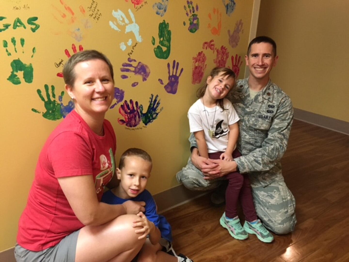 The Daniels family pose in front of the radiation treatment room’s victory wall, with the hand prints of everyone who has gone through treatment in that room. The Daniels family’s hand prints are between them.