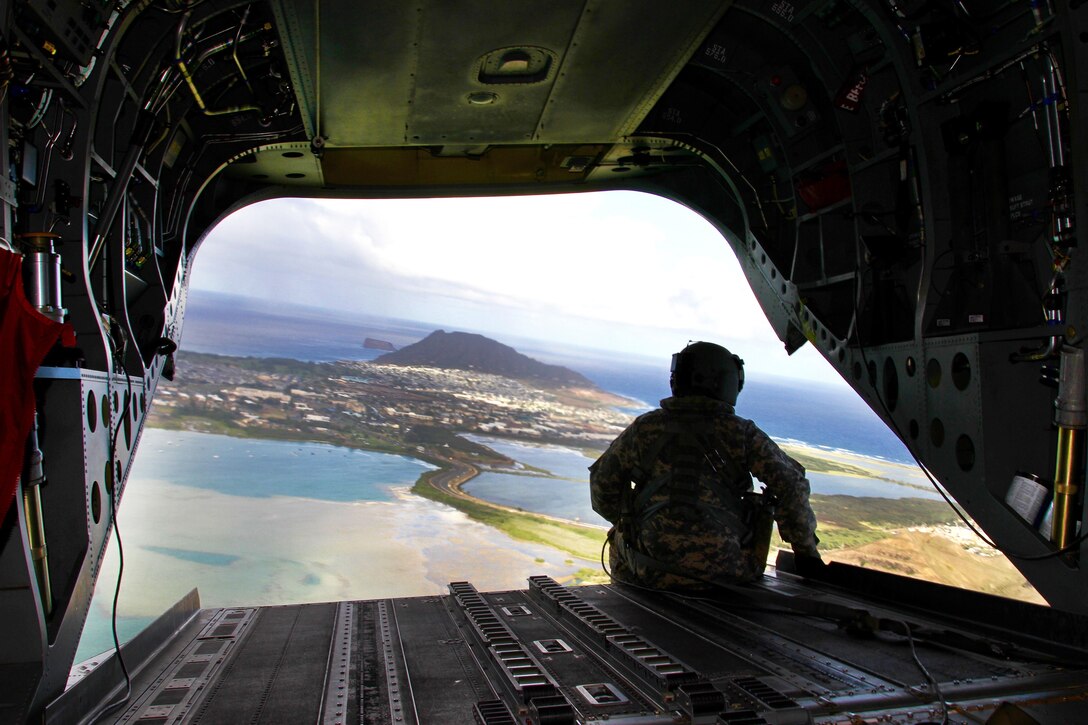 An Army crew chief looks out the back of a CH-47 Chinook helicopter at an island view after participating in low-altitude air drops near Bellows Air Force Base, Hawaii, Jan. 25, 2017. Army photo by Sgt. Ian Ives