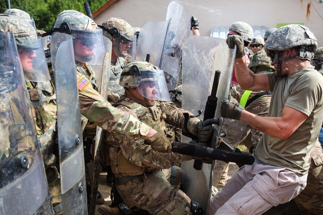 A U.S. soldier, center, prevents another U.S. soldier role-playing as a hostile civilian from taking his riot shield while conducting a riot control scenario during a Kosovo Force mission rehearsal exercise at the Joint Multinational Readiness Center in Hohenfels, Germany, June 30, 2017. Army photo by Spc. Randy Wren