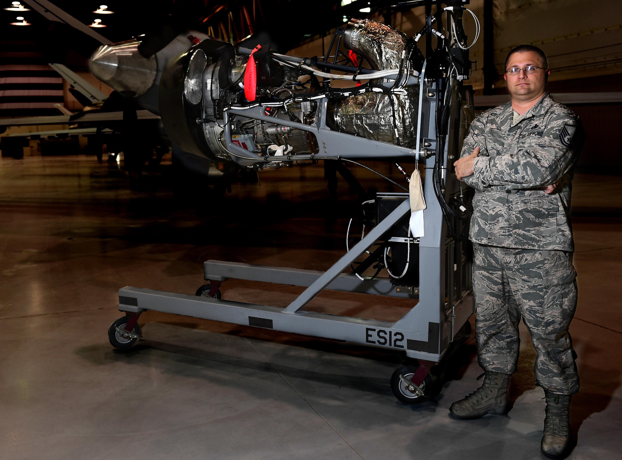 Master Sgt. Eric, 432nd Aircraft Maintenance Squadron Reaper Aircraft Maintenance Unit production superintendent, stands with the engine trainer he created June 19, 2017, at Creech Air Force Base, Nev. He saw a need to have a power capable training engine to practice engine rigging, which involves tuning the actuators that translate electrical signals to mechanical commands. If done improperly the engine can shutoff when not intended. The trainer allowed maintainers to train on this vital task without taking an operational aircraft out of the rotation. (U.S. Air Force photo/Senior Airman Christian Clausen) 