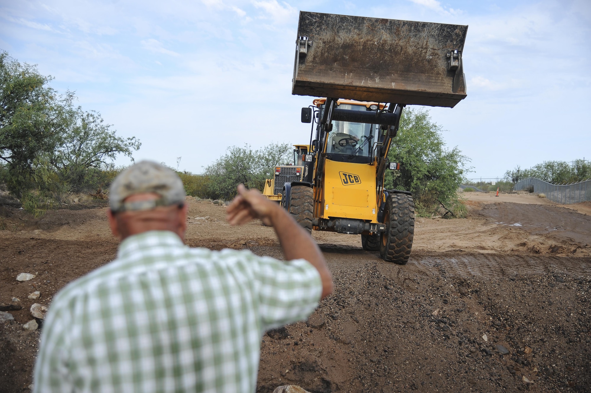 Douglas Burke, 355th Civil Engineer Squadron heavy equipment operator, directs an Airman utilizing a front-end roller at Davis-Monthan Air Force Base, Ariz., June 8, 2017. These 355th CES Airmen were reconstructing a permanent foundation for Atterbury Wash, a key element to the monsoon season for the installation and local Tucson community. (U.S. Air Force photo by Senior Airman Mya M. Crosby)