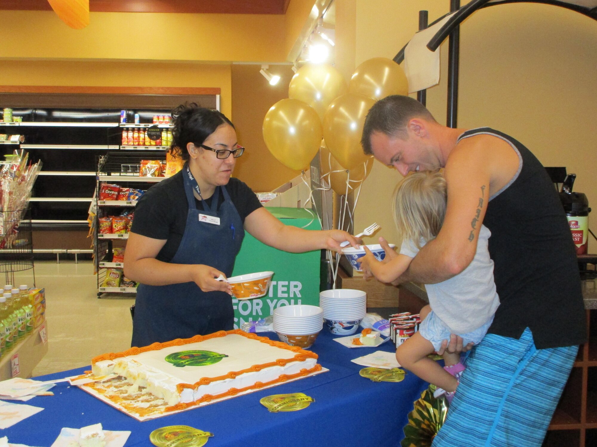 Wignelia Cruz-Gonzalez, Laughlin Commissary produce manager, gives a slice of cake to a military child at Laughlin Air Force Base, Tx., July 1. To observe the commissary’s 150th birthday, Laughlin’s commissary staff handed out free cake and reduced its store prices on food and household goods. 