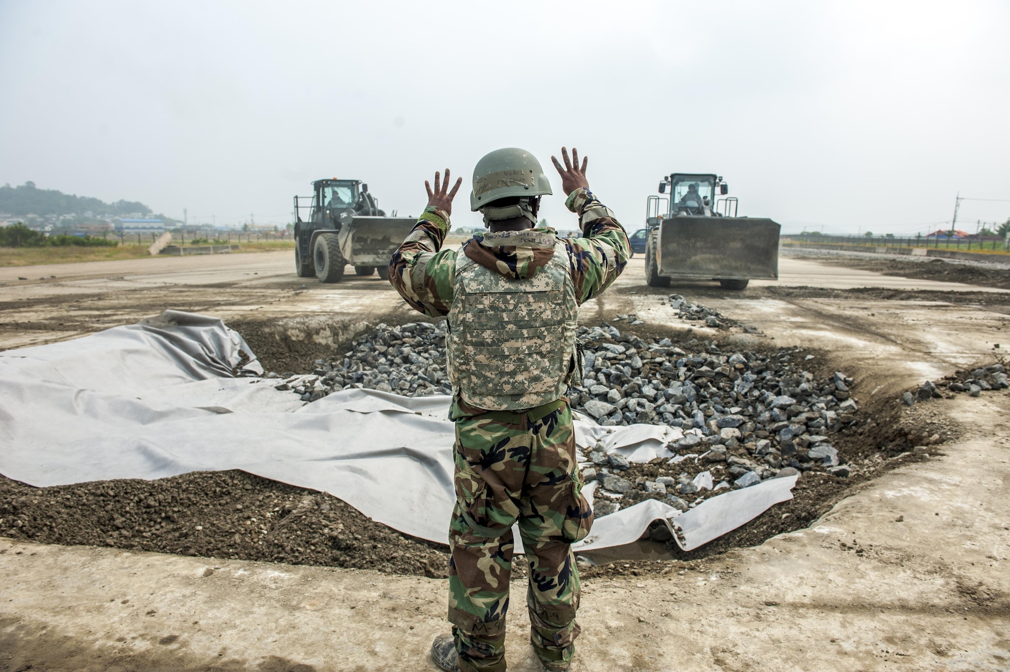 U.S. Air Force Tech. Sgt. Freeman Gleaves, 8th Civil Engineering Squadron pavement and construction craftsman, communicates with two loaders June 29, 2017, at Kunsan Air Base, Republic of Korea. The CES Airmen were tasked with repairing a damaged portion of the runway while participating in an airfield damage repair exercise. (U.S. Air Force photo by Senior Airman Colville McFee/Released)