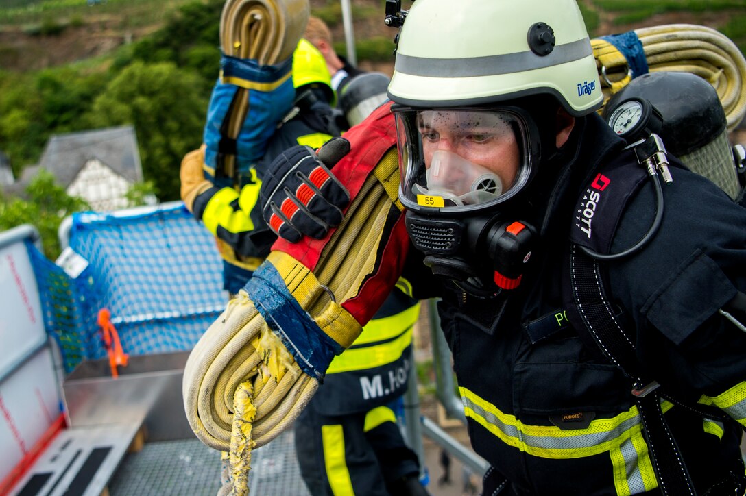 A firefighter from Germany carries a hose while racing against an opponent during the 4th annual Mosel Firefighter Combat Challenge in Ediger-Eller, Germany, June 30, 2017. During the first obstacle of the competition, a 42 pound hose must be carried up a five-story tower with fire protective gear on including gloves, mask, helmet, coat, pants, boots and an air pack. (U.S. Air Force photo by Senior Airman Preston Cherry)