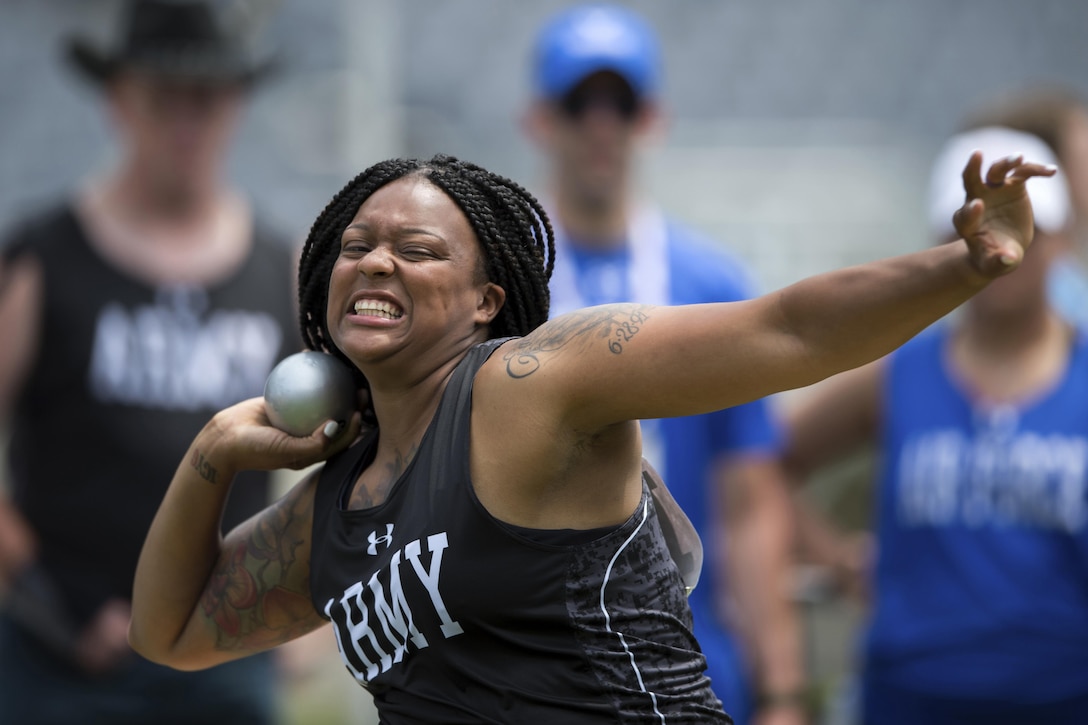 A soldier throws a shot put while seated during competition.