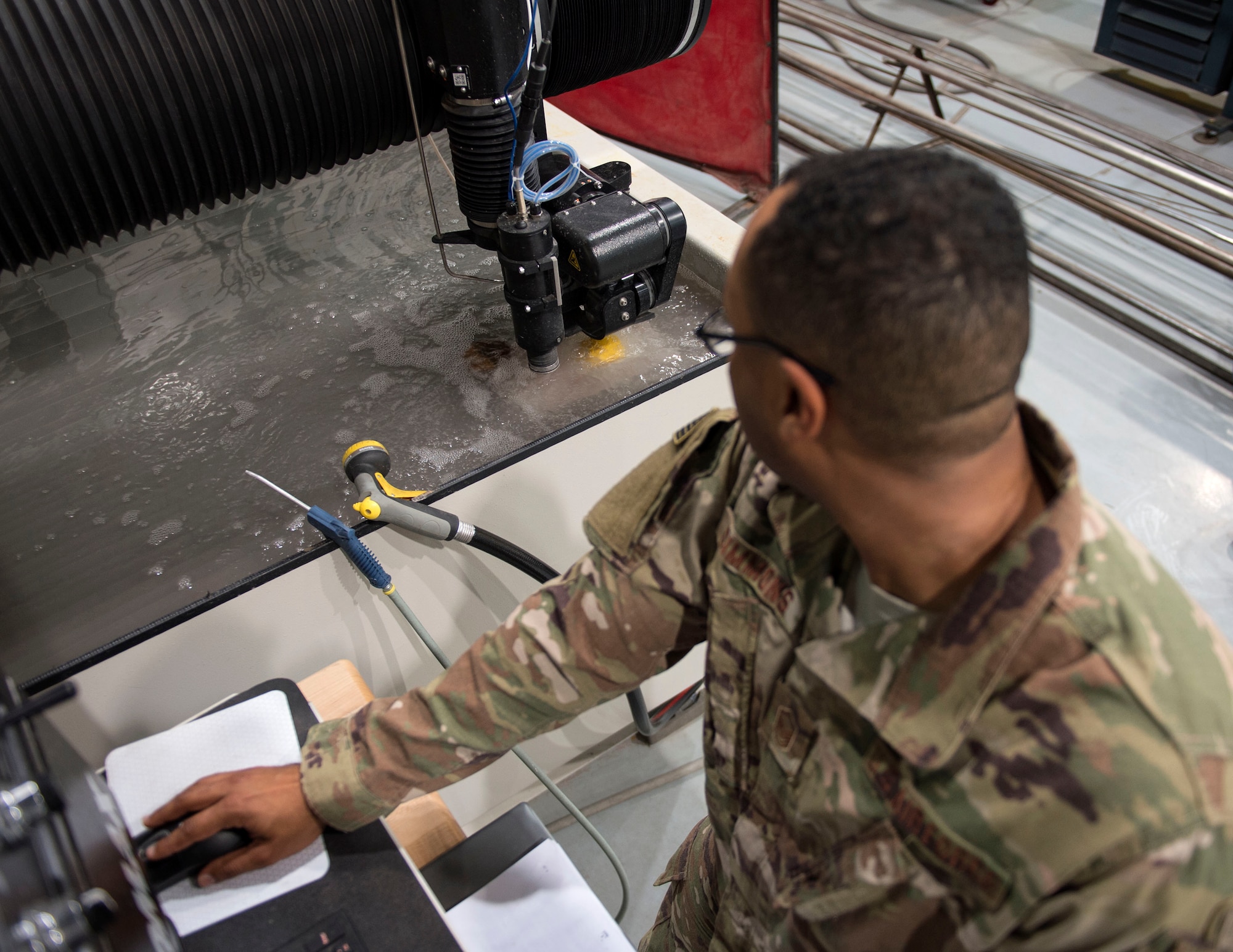 U.S. Air Force Master Sgt. Anwar Simmons, section chief with the 379th Expeditionary Maintenance Squadron, watches the abrasive waterjet cutting machine at Al Udeid Air Base, Qatar, May 30, 2017. The abrasive waterjet cutting machine allows the airmen to create a wide range of aircraft parts or tools needed to complete the mission in an expedited and a cost effective manner. (U.S. Air Force photo by Tech. Sgt. Amy M. Lovgren)