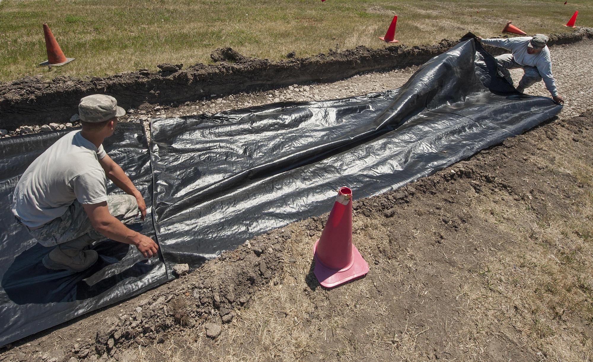 From left, Airman 1st Class Christopher Schroeder and Senior Airman Thomas Clark, 5th Civil Engineer Squadron pavements and equipment technicians, cover geotextile over the ground at Minot Air Force Base, N.D., June 12, 2017. Geotextiles are permeable fabrics used in conjunction with soil to separate, filter, reinforce, protect and drain water. (U.S. Air Force photo by Airman 1st Class Jonathan McElderry)