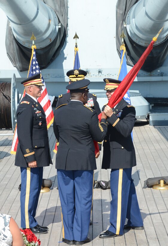 Under the big guns onboard the Battleship U.S.S. North Carolina, incoming commander Col. Robert J. Clark, right, passes the U.S. Army Corps of Engineers flag to South Atlantic Division (SAD) Command Sergeant Major Douglas S. Padgett during the Wilmington District's change of command ceremony as outgoing commander Col. Kevin P. Landers, Sr., left, and SAD Commander Brig. Gen. C. David Turner, rear, look on. Col. Clark comes to the Wilmington District after attending the U.S. Army War College in Carlisle Barracks, Pennsylvania, where he earned a Master’s Degree in Strategic Studies. 