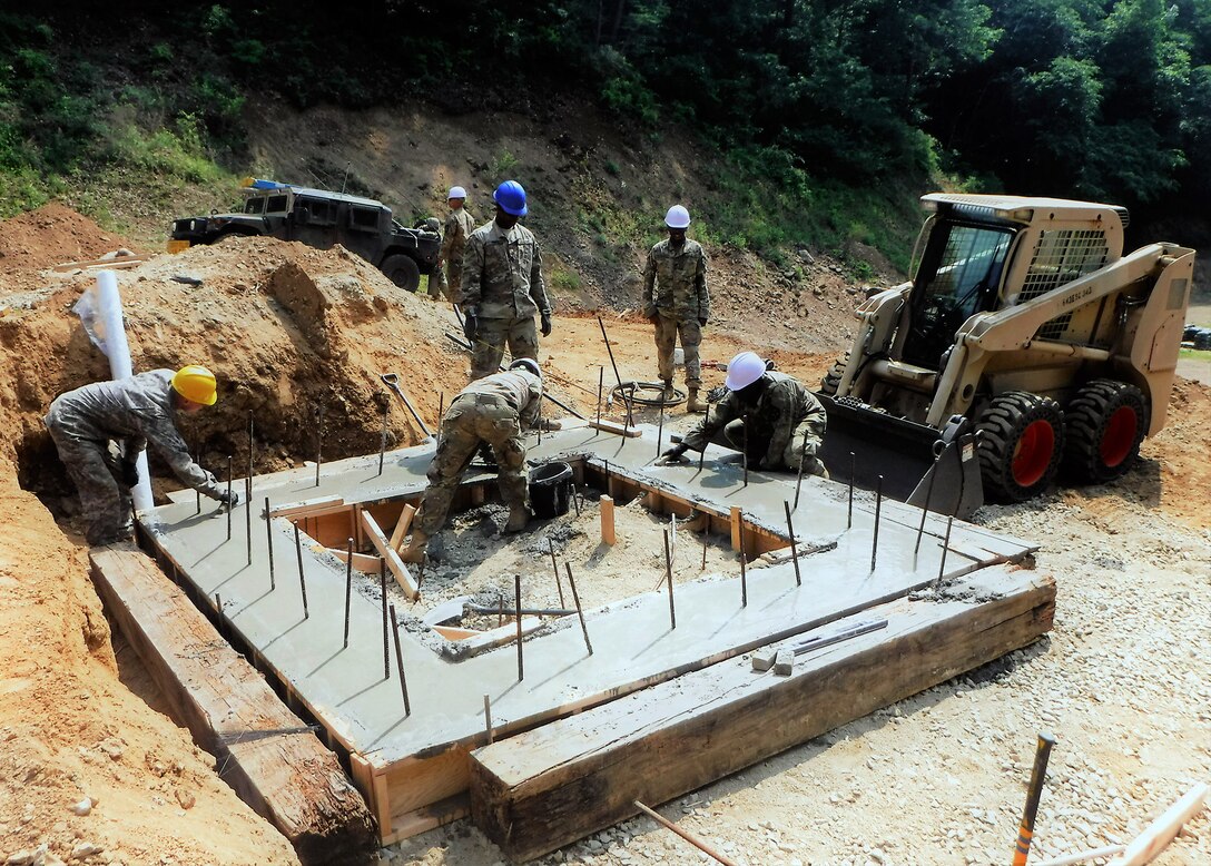 Team leader Sgt. Eric Dubard (standing, blue helmet) supervises his Soldiers as they smooth the newly poured concrete for a grenade bunker at Arapaho Range.