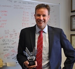 DAHLGREN, Va. (July 7, 2017) – Kris Parker, Naval Surface Warfare Center Dahlgren Division (NSWCDD) deputy for small business, is inspired by a quote – written on his whiteboard in the background – spoken by Sir Michael Gambon in Matthew Vaughn's Layer Cake: "The art of good business is being a good middleman". Parker is holding the Department of the Navy Office of Small Business Program Award for NSWCDD’s first-time achievement of a statutory small business goal – three percent of total contracted dollars to service disabled veteran owned small businesses.  

DON Office of Small Business Programs, small business, Naval Surface Warfare Center Dahlgren Division, NSWCDD, Service Disabled Veteran Owned Small Business Contracts, Disabled Veterans, Veteran Owned Small Business, Statutory Goal Achievement Award, Statutory Goal 
