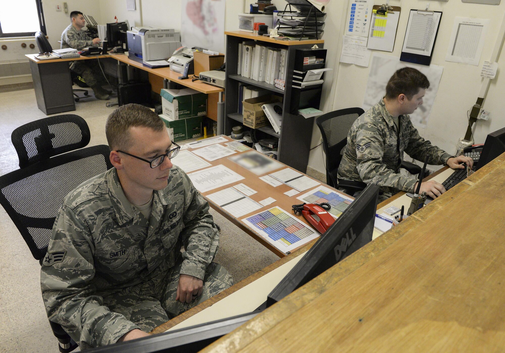 U.S. Air Force Senior Airmen Thomas Smith, foreground left, and William Terry, foreground right, airfield management shift leads and Tech. Sgt. Santino Sustaita, airfield driving program manager, background, all assigned to the 379th Expeditionary Office of Strategic Services, work on their computers at Al Udeid, Air Force Base, Qatar, June 7, 2017. Airfield Management oversees more than 20 million square feet of airfield at Al Udeid in addition to overseeing the airfield driving program and filing all flight plans for flights arriving to and departing from the base. (U.S. Air National Guard photo by Tech. Sgt. Bradly A. Schneider/Released)