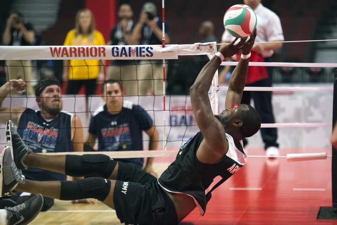 An army veteran reaches for a volleyball seated on the floor.