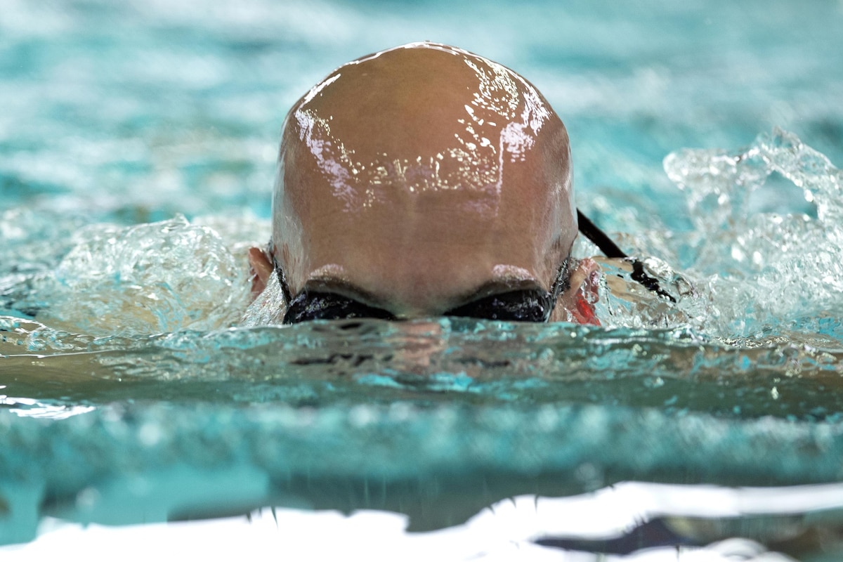 A sailor with half his bald head submerged swims the breaststroke.