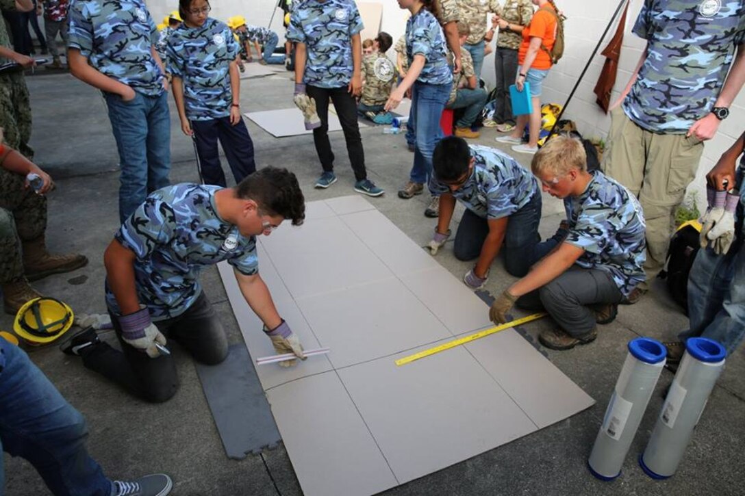 From June 17 to June 21, 2017 high school students from the Society of American Military Engineers (SAME) spent a week at Courthouse Bay, Camp Lejeune, N.C. participating in various engineer themed activities. Here a group of students are measuring and scoring cardboard in order to assist in shaping their cardboard amphibious vehicles.  Once the amphibious vehicles are complete they will be tested in a shallow inlet. 