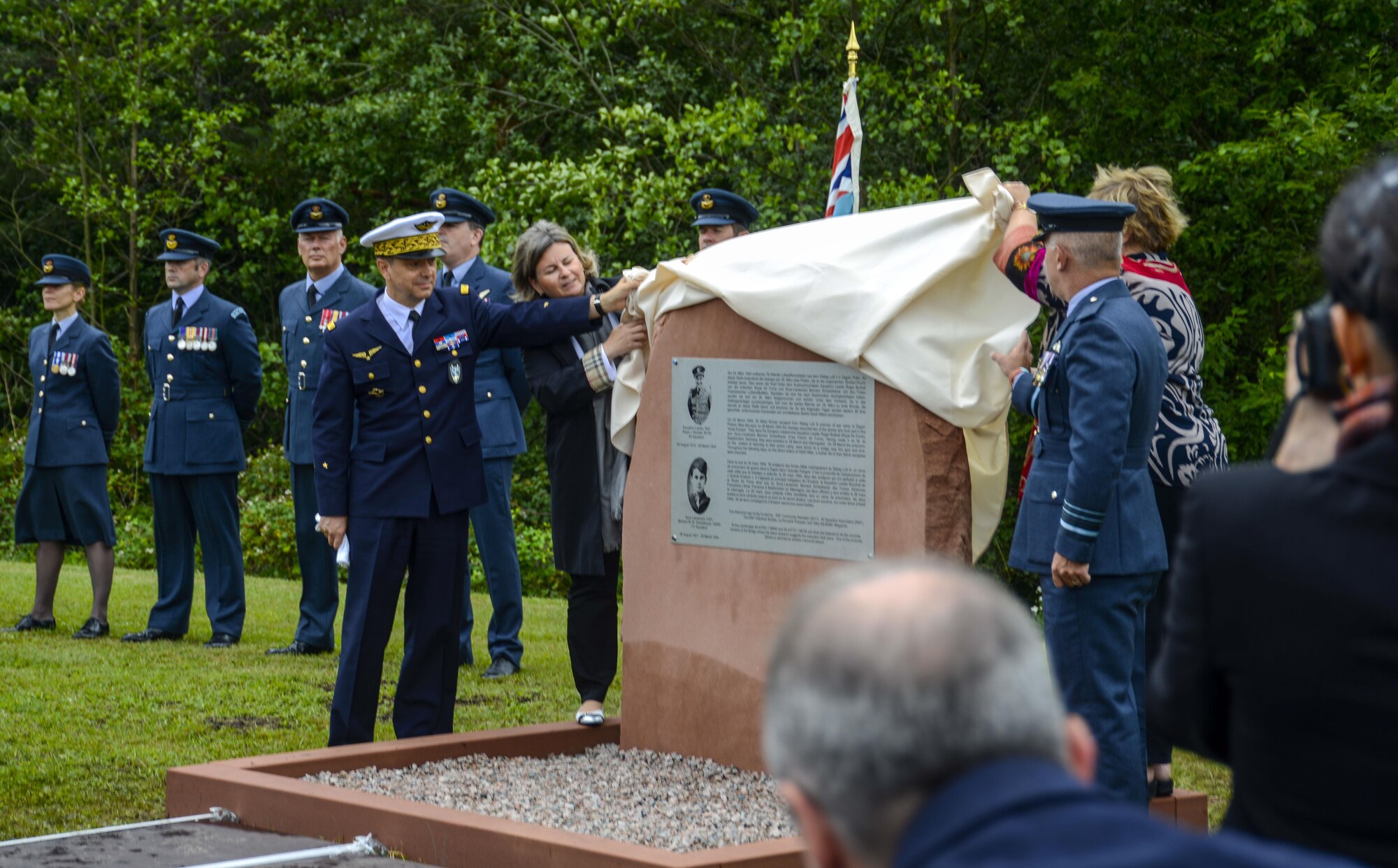 Members of the French and Royal Air Forces assist family members of Squadron Leader Roger Bushell, Royal Air Force, and Sous-Lieutenant Bernard Scheidhauer, Free French Air Force, unveil the memorial dedicated to the two men outside the West Gate of Ramstein Air Base, Germany, July 1, 2017. The two airmen were the masterminds behind the “Great Escape” that took place March 24, 1944. During the Escape, 76 Allied airmen escaped from the prisoner of war camp Stalag Luft III at Żagań, Poland. Although, they only made it as far as Saarbrücken, Germany, they were arrested on March 26, and interrogated. On March 29, under the pretext of being returned to their prison camp, Bushell and Scheidhauer were driven to a bridge near Ramstein and killed. Throughout the following days, 48 of their fellow escapees were executed. The commemorative stone was made possible through the support and efforts of the German, U.S., British, and French communities. (U.S. Air Force photo by Staff Sgt. Timothy Moore)