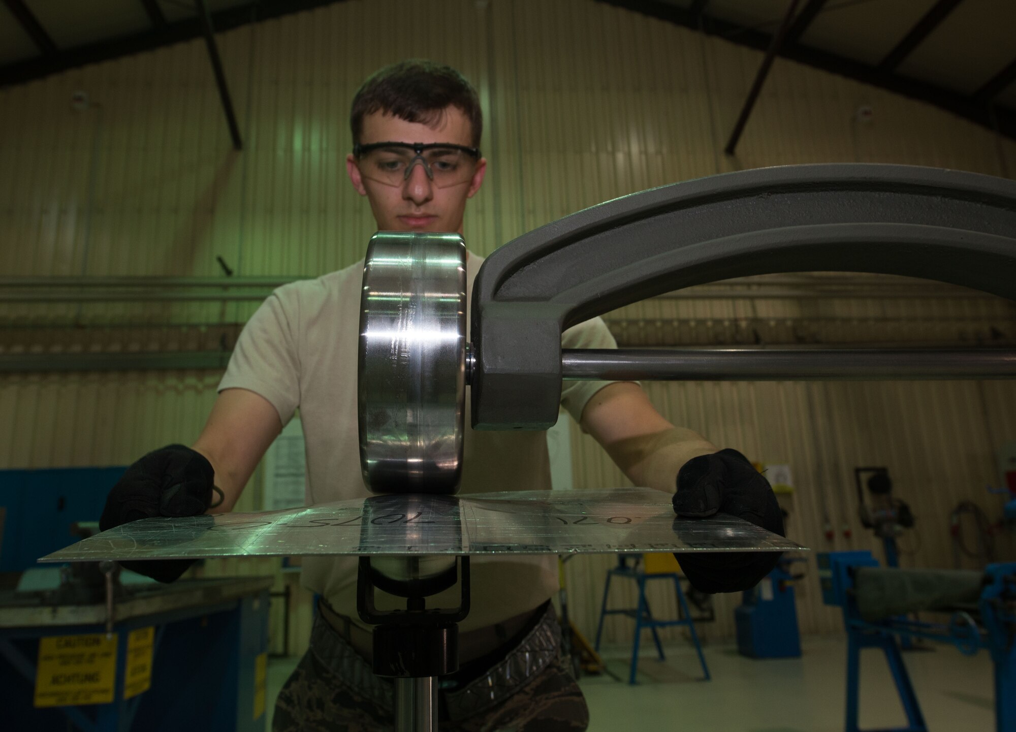 U.S. Air Force Senior Airman Ian Michaels, 86th Maintenance Squadron aircraft structural maintenance journeyman, rolls a piece of metal through a machine to give it curvature on Ramstein Air Base, Germany, July 5, 2017.  The aircraft structural maintenance shop uses machines like the roller to give aircraft parts, such as hull and wing pieces, the precise curvature to replace damaged parts. (U.S. Air Force photo by Senior Airman Elizabeth Baker)