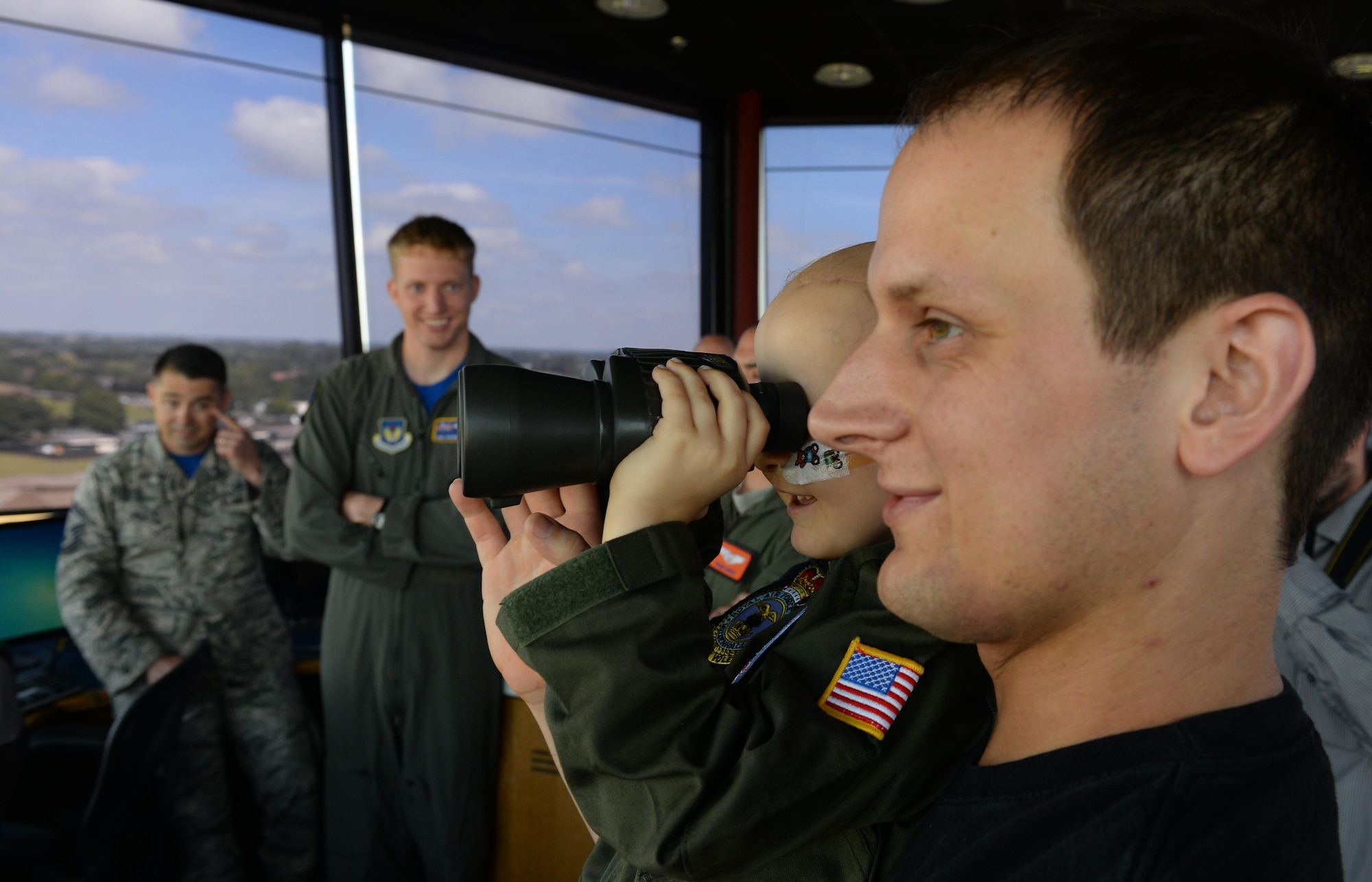 Martin Davidson, holds his son, Jay, while he looks through binoculars in the air traffic control tower during a Pilot for a Day visit July 7, 2017, on RAF Mildenhall, England. Jay was diagnosed with high-risk medulloblastoma in January 2017 and was offered the opportunity to visit the base to view aircraft and meet aircrew. (U.S. Air Force photo by Staff Sgt. Micaiah Anthony)