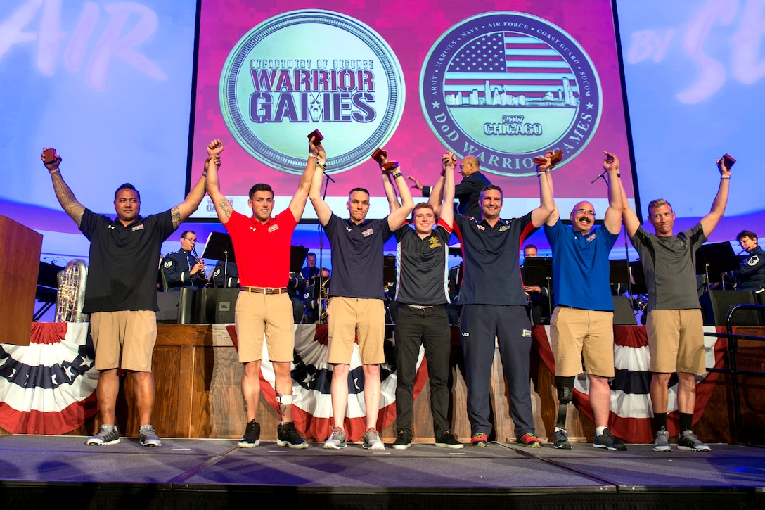 Team representatives raise each other's arms on stage during a ceremony.