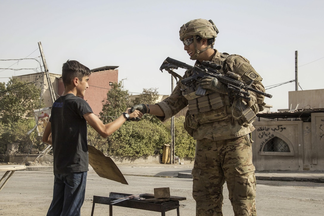 A soldier shakes the hand of a young boy while patrolling to support Operation Inherent Resolve in Mosul, Iraq, July 4, 2017. The soldier is a paratrooper assigned to the 82nd Airborne Division's 2nd Brigade Combat Team. Army photo by Cpl. Rachel Diehm