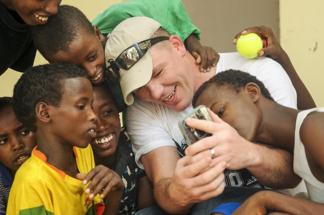 Army Spc. Rodney Drew takes a picture with children at Caritas, a facility that provides meals and medical care to youth in Djibouti, July 06, 2017. Drew is assigned to Company B, 1st Battalion, 153rd Infantry Regiment. Army National Guard photo by Spc. Victoria Eckert