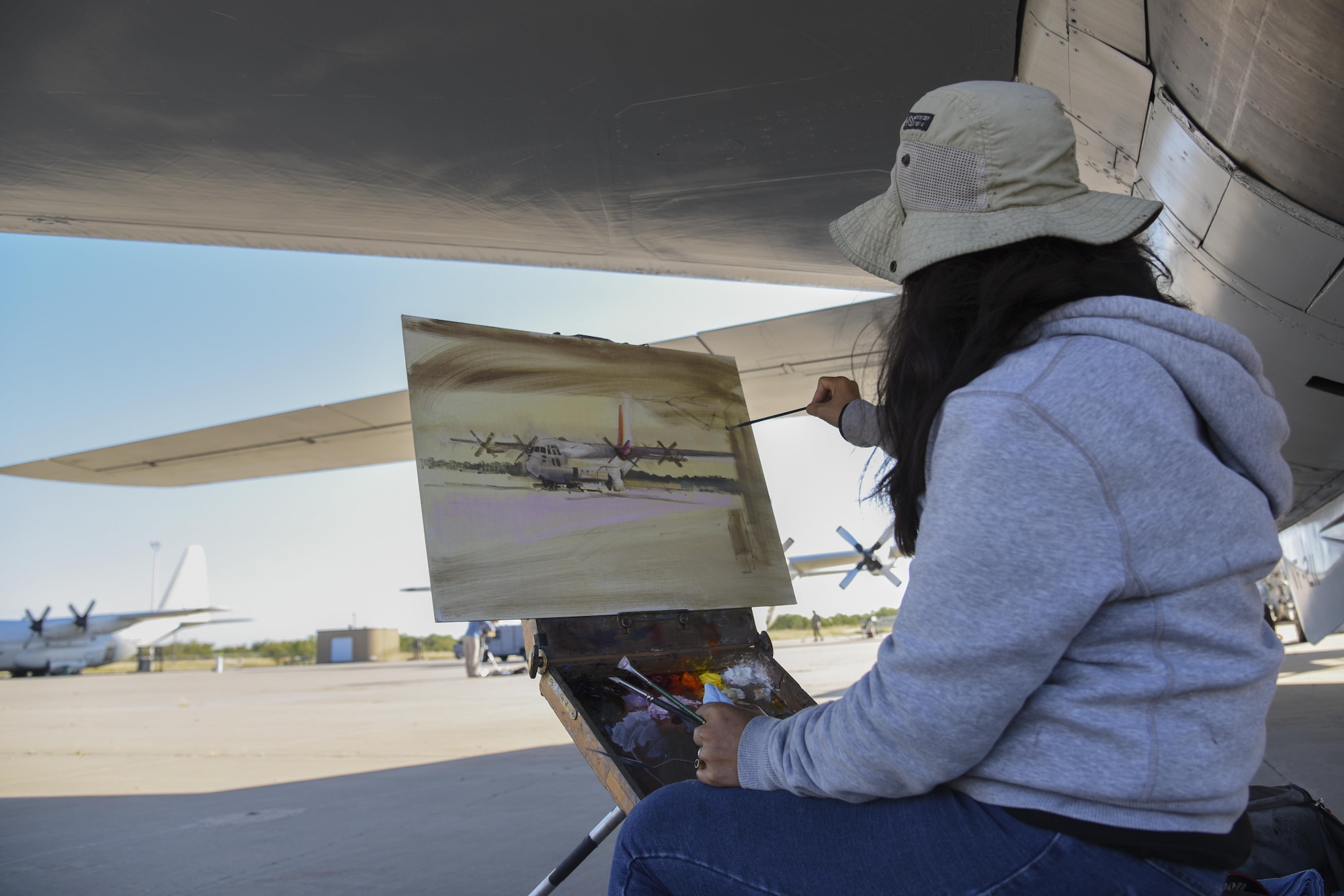 Hiu Lai Chong, artist, paints a C-130 at the Louis F. Garland Department of Defense Fire Academy on Goodfellow Air Force Base, Texas, Oct. 26, 2016. Chong was painting the C-130 as part of the EnPleinAirTEXAS competition in San Angelo, Texas. (U.S. Air Force photo by Staff Sgt. Joshua Edwards/Released)