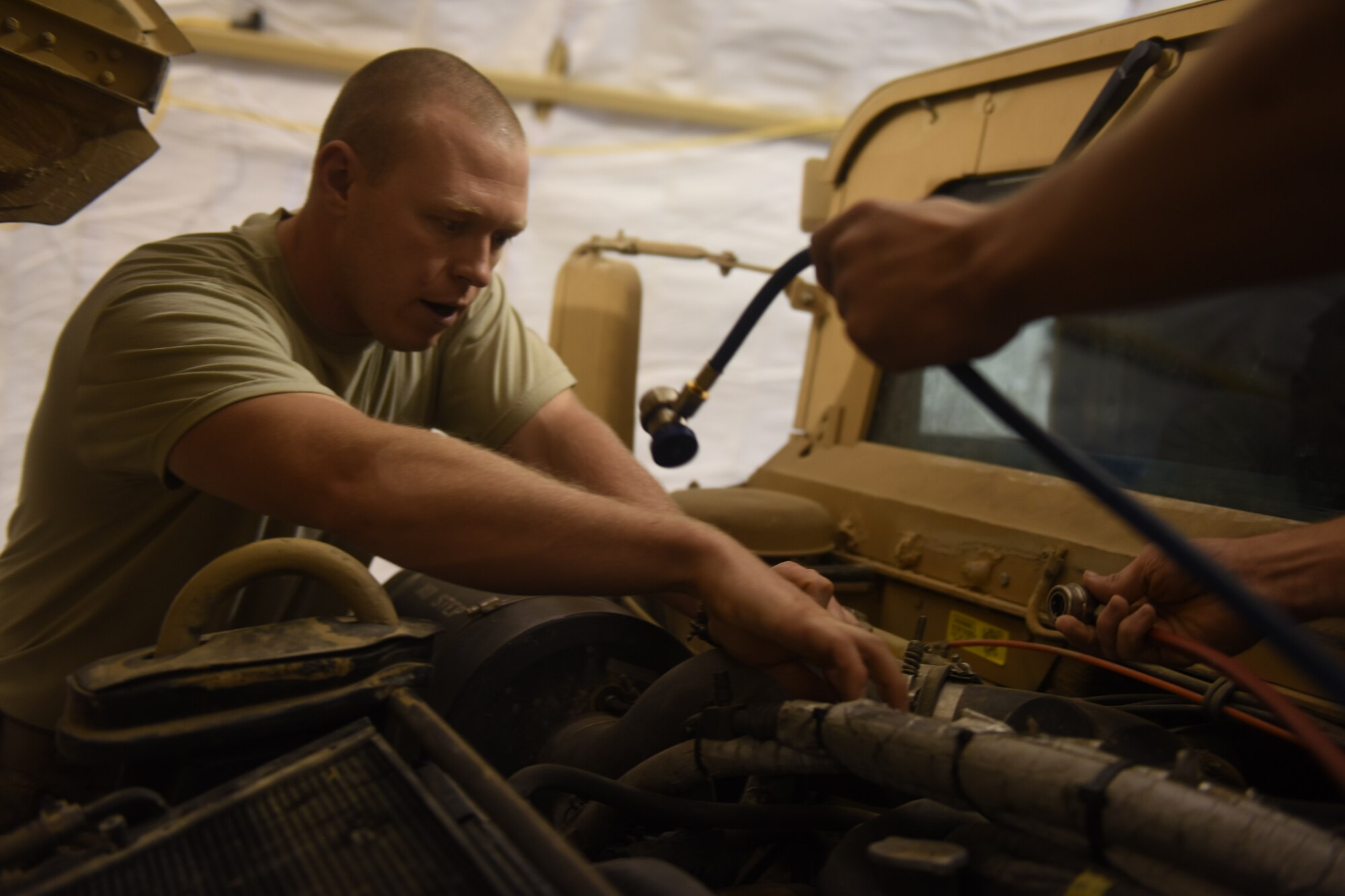 U.S. Air Force Staff Sgts. Shawn Benton, an aerospace ground equipment craftsman, and. Adam Martin, a fire truck maintenance specialist, both deployed in support of Combined Joint Task Force – Operation Inherent Resolve and assigned to the 370th Air Expeditionary Advisory Group, Detachment 1, work together to charge the air conditioning system of a Humvee at Qayyarah West Airfield, Iraq, July 2, 2017. Benton often works outside of his scope to assist with vehicle maintenance and facility sustainment at the Air Force compound at Qayyarah West CJTF-OIR is the global Coalition to defeat ISIS in Iraq and Syria. (U.S. Air Force photo by Tech. Sgt. Jonathan Hehnly)